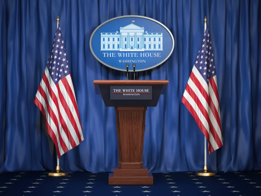 A White House podium flanked by two United States flags.