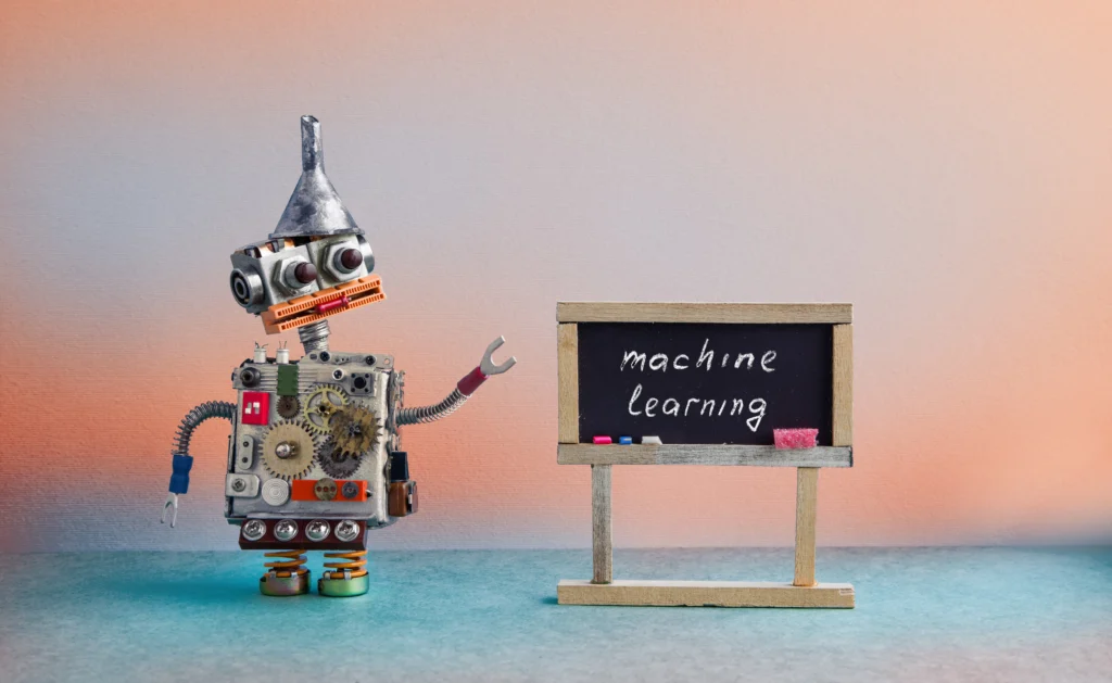 A robot points to a blackboard. Writing on the board reads 'macine learning'.