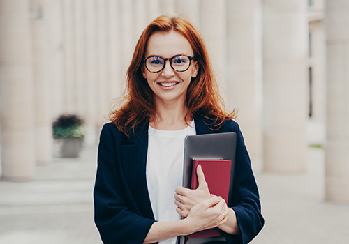 A professional stands outside a government building and carries writing resources for their government job.