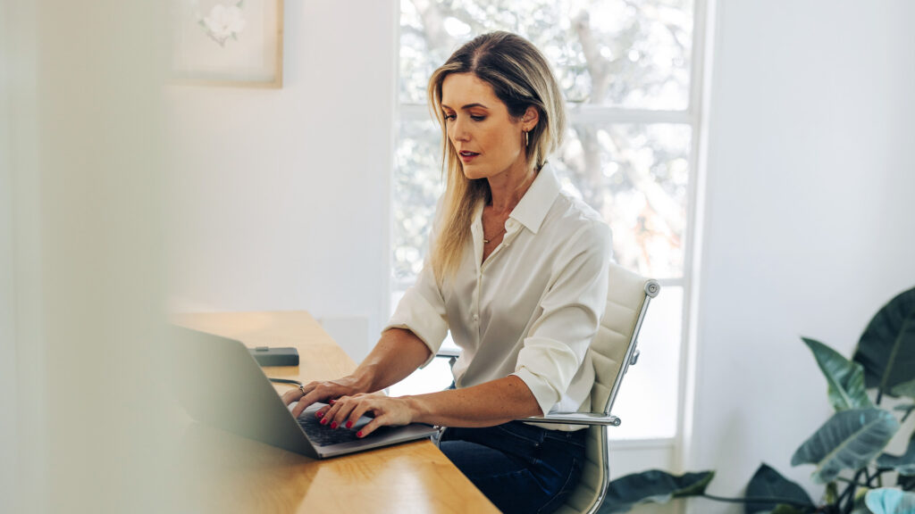 A woman is sitting in her office, typing on her laptop