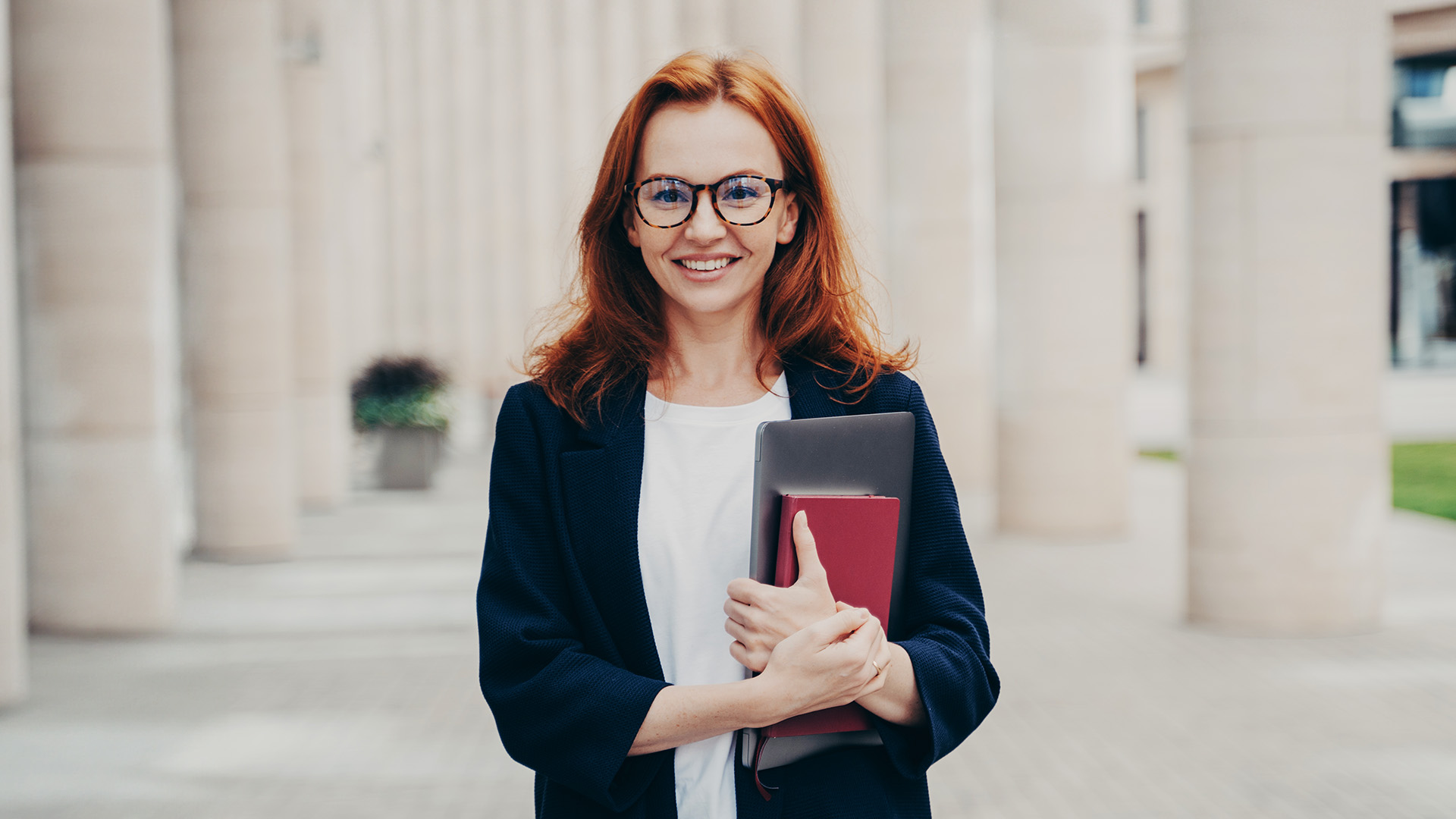 A professional stands outside a government building and carries writing resources for their government job.